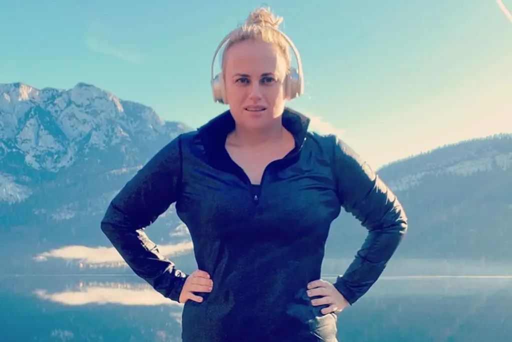 Rebel Wilson wearing track suit and headphones on a hill working out for her weight loss.